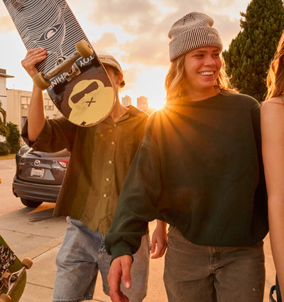 A group of people walking on the street at sunset holding skate boards. 