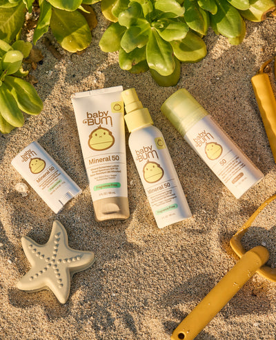 Baby sunscreen products on sand with greenery