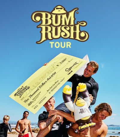 A beach scene with several men celebrating outdoors under a large 'Bum Rush Tour' logo. One man holds a oversized novelty check, while another holds a small cartoon mascot figure.