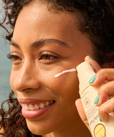 Woman applying sunscreen cream to her face with a clear background