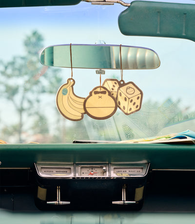 Decorative rearview mirror with banana, pineapple, and dice design hanging from a car's rearview mirror.