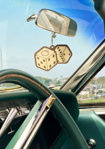 Car interior with a rearview mirror and dice decorations on a sunny day.