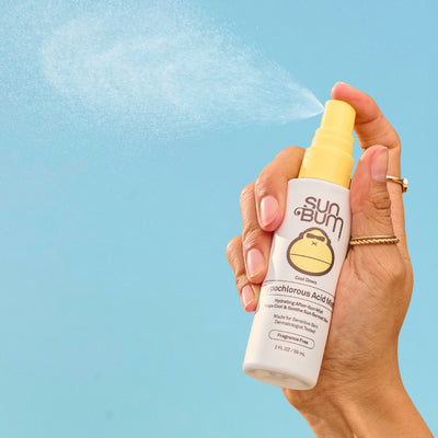 Hand holding a Sun Bum spray bottle against a blue background