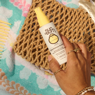 Hand holding a Sun Bum bottle on a textured surface with floral patterns