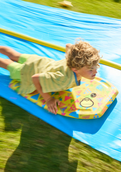 Child lying on a colorful inflatable mat with a slide on grass