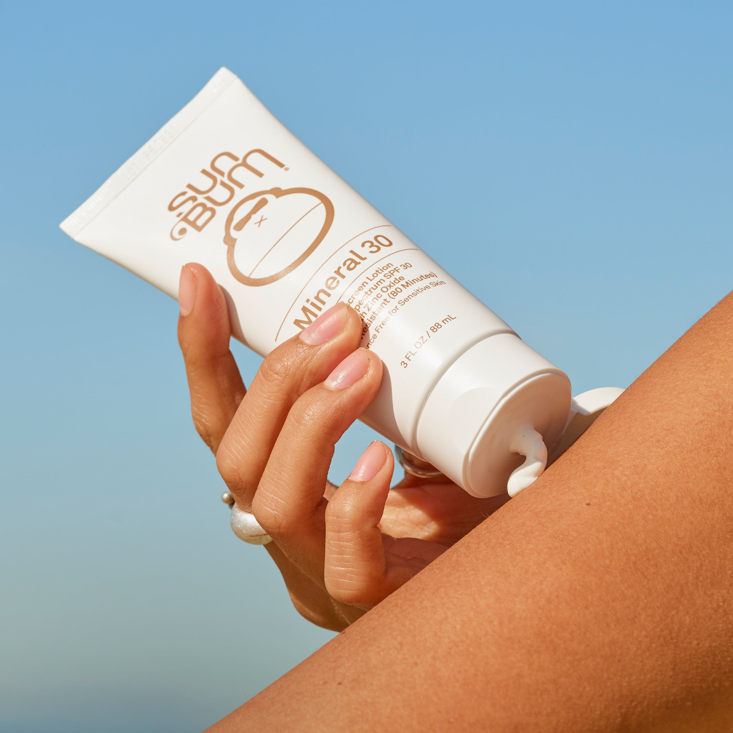 Hand applying sunscreen cream to arm with a clear blue sky background