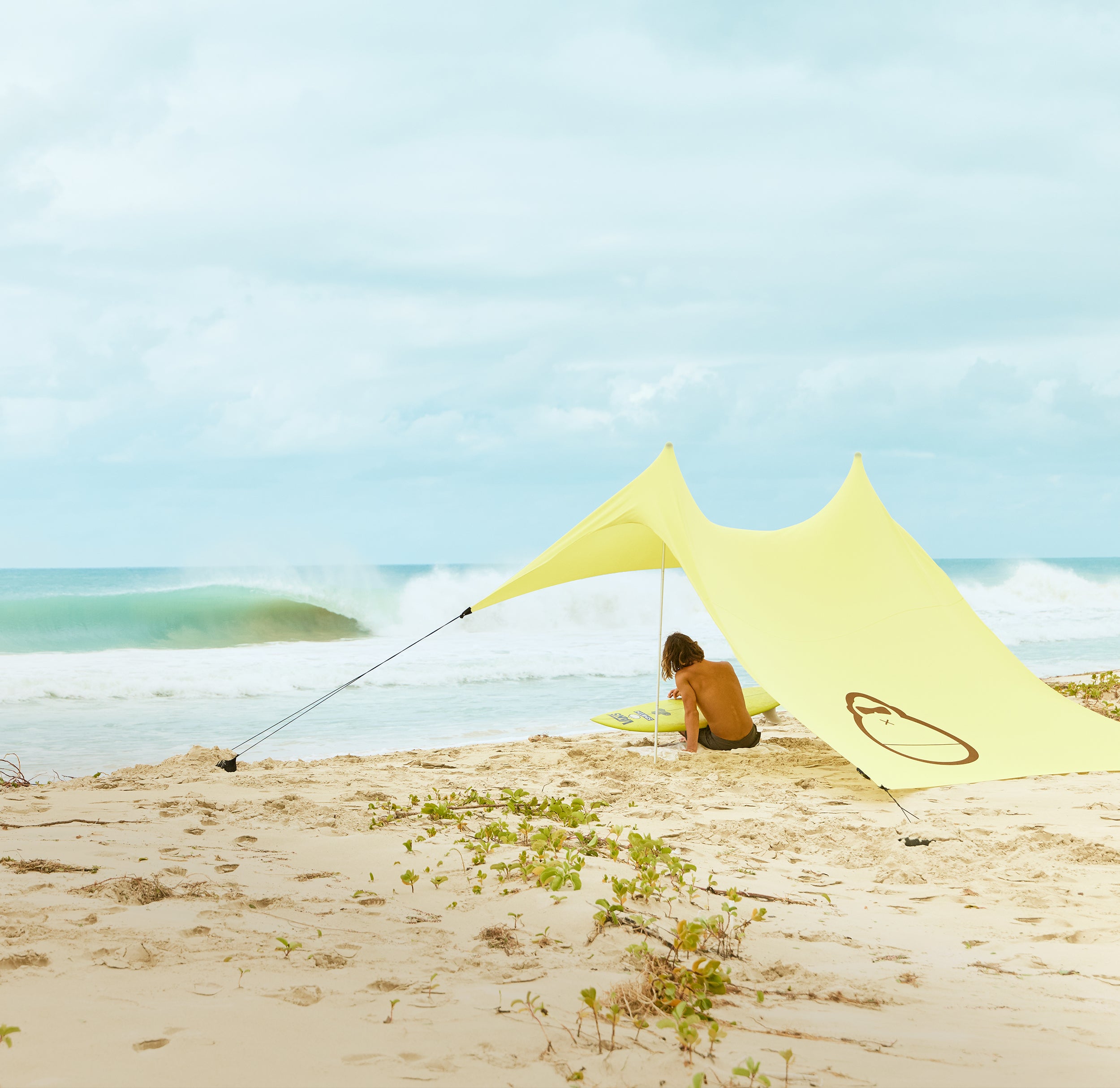 Person sitting under a yellow canopy on a sandy beach with ocean waves in the background