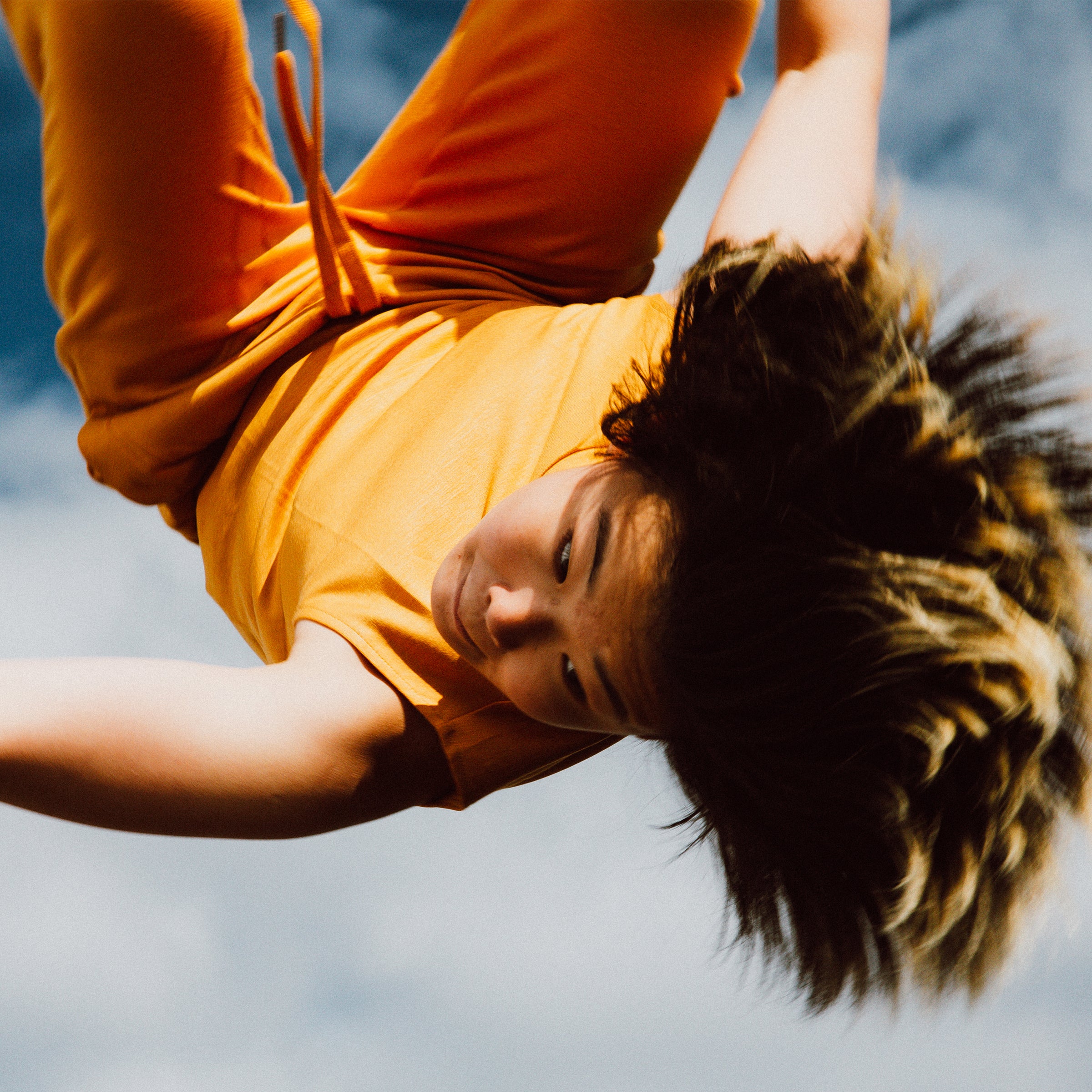 Person in an orange shirt upside down against a blue sky