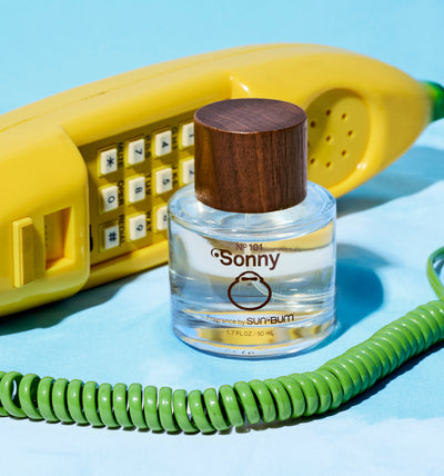 Small bottle of 'Sonny' perfume with a wooden cap, yellow phone, and green cord on a blue background