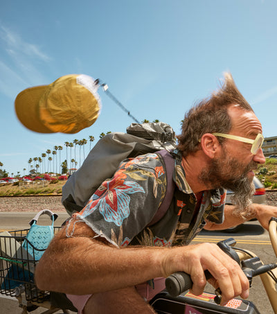 Man riding a motorcycle with a yellow cap in the air, palm trees and clear sky in the background