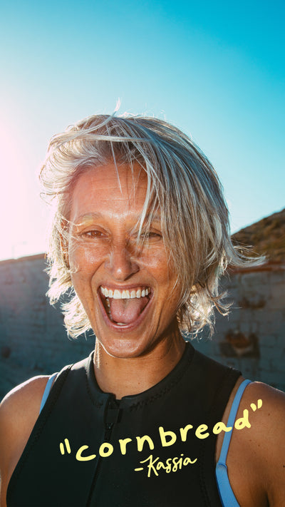 Person with light-colored hair and a black sleeveless top with 'cornbread' quote, set against a bright blue sky.