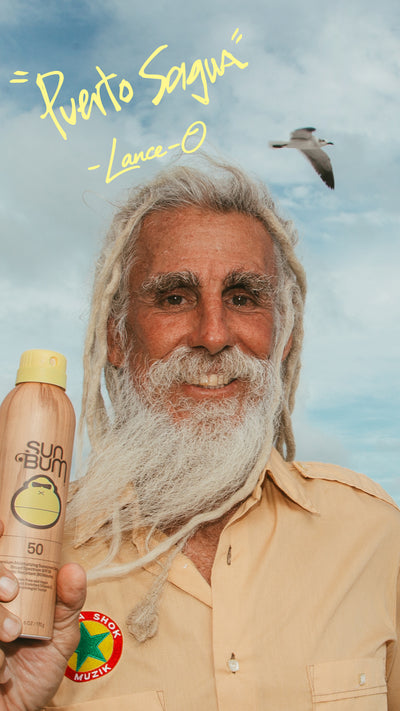 Man with a beard holding a Sun Bum sunscreen bottle against a blue sky with a seagull and the quote "puerto sagua" 