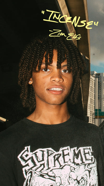 Person wearing a black Supreme t-shirt with quote that says "incense" and cityscape background