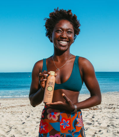 Woman on a beach holding a bottle of sunscreen