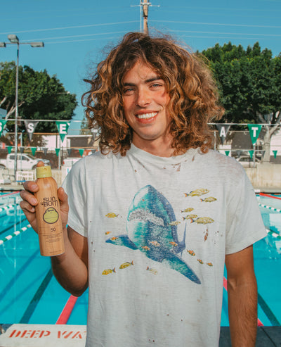 Person holding a Sun Bum sunscreen bottle by a pool