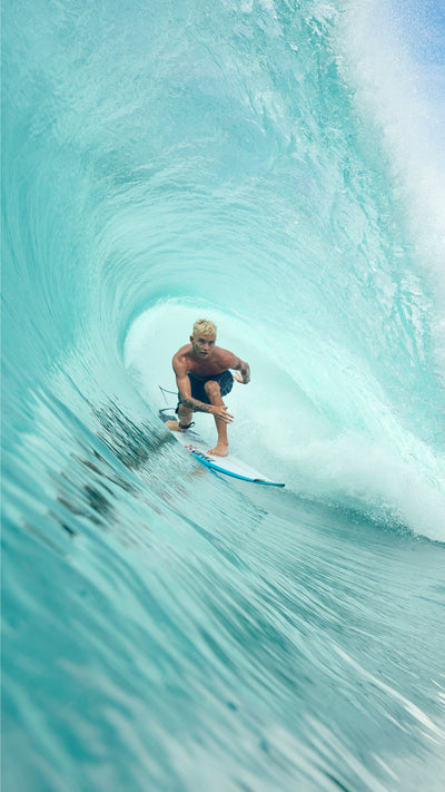 Person surfing inside a barrel wave in crystal clear blue water