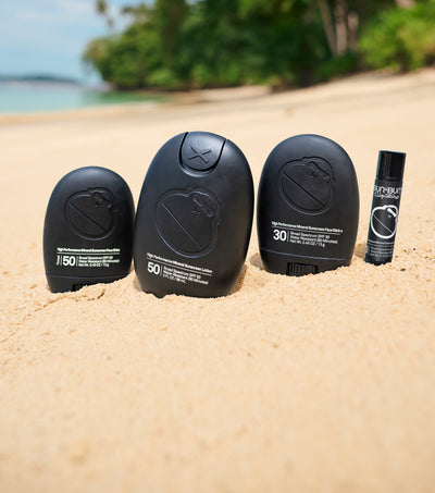 Four black sunscreen bottles with different SPF levels on a sandy beach.
