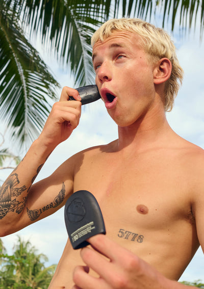 Man with tattoos applying signature sunscreen against a tropical background