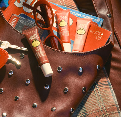 Lip balm tubes on a studded brown leather bag with sunglasses and keys.
