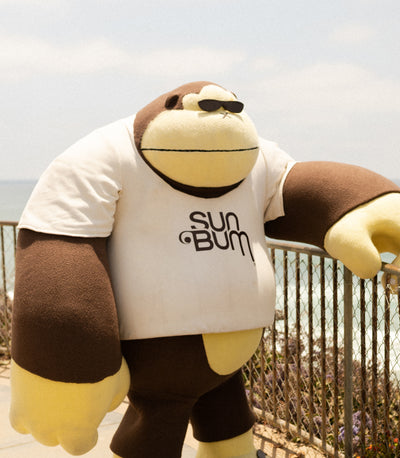 Sonny mascot chillin' oceanside in shades and Sun Bum tee, radiating laid-back beach vibes - Ask The Bum Collection - Sun Bum