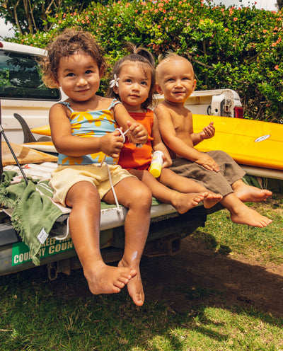 Three toddlers on a truck tailgate with surfboards, smiling and holding Baby Bum sunscreen - Baby Bum Collection - Sun Bum
