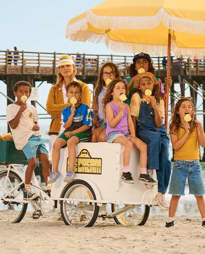 Group of kids enjoying ice cream on a beach under a yellow umbrella by a Sun Bum cart - Kids Collection - Sun Bum