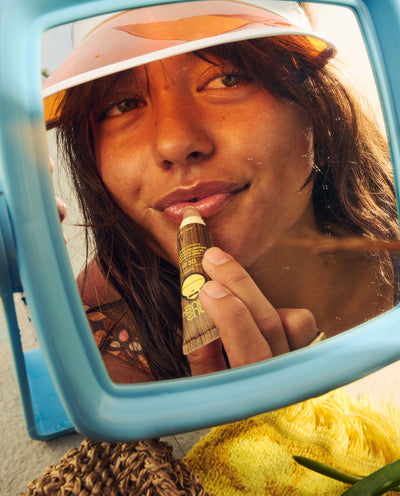 Woman applying SPF 30 lip balm while looking into a mirror during a sunny day - Lip Collection - Sun Bum