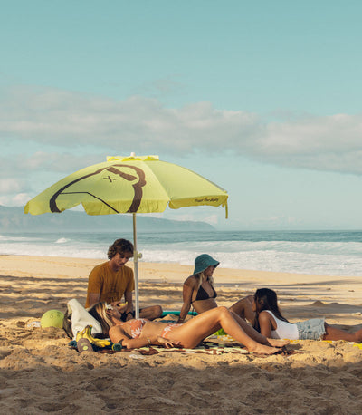 People relaxing under a yellow umbrella on a beach with ocean in the background