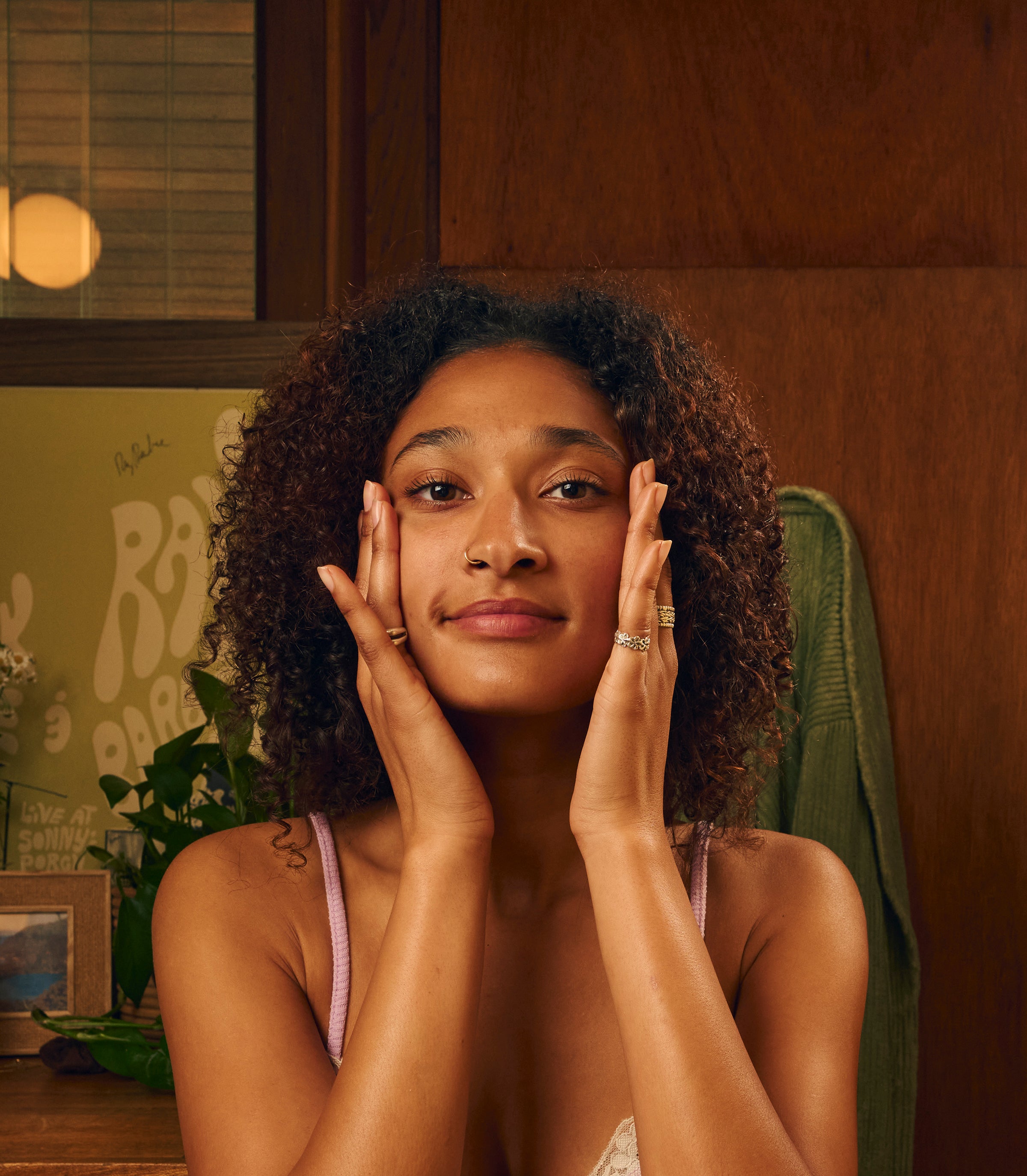 Woman gently massaging her face in a cozy room, highlighting her skincare routine from the SB Face Collection – Sun Bum.