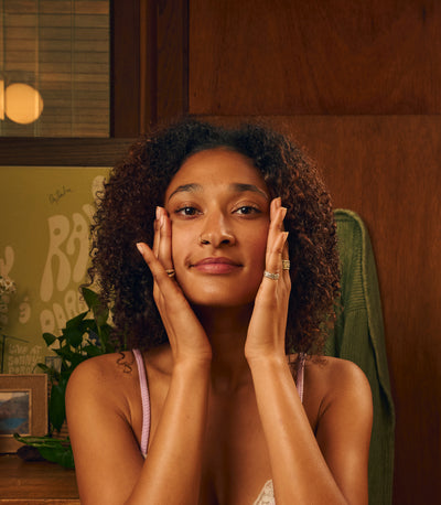 Woman gently massaging her face in a cozy room, highlighting her skincare routine from the SB Face Collection – Sun Bum.