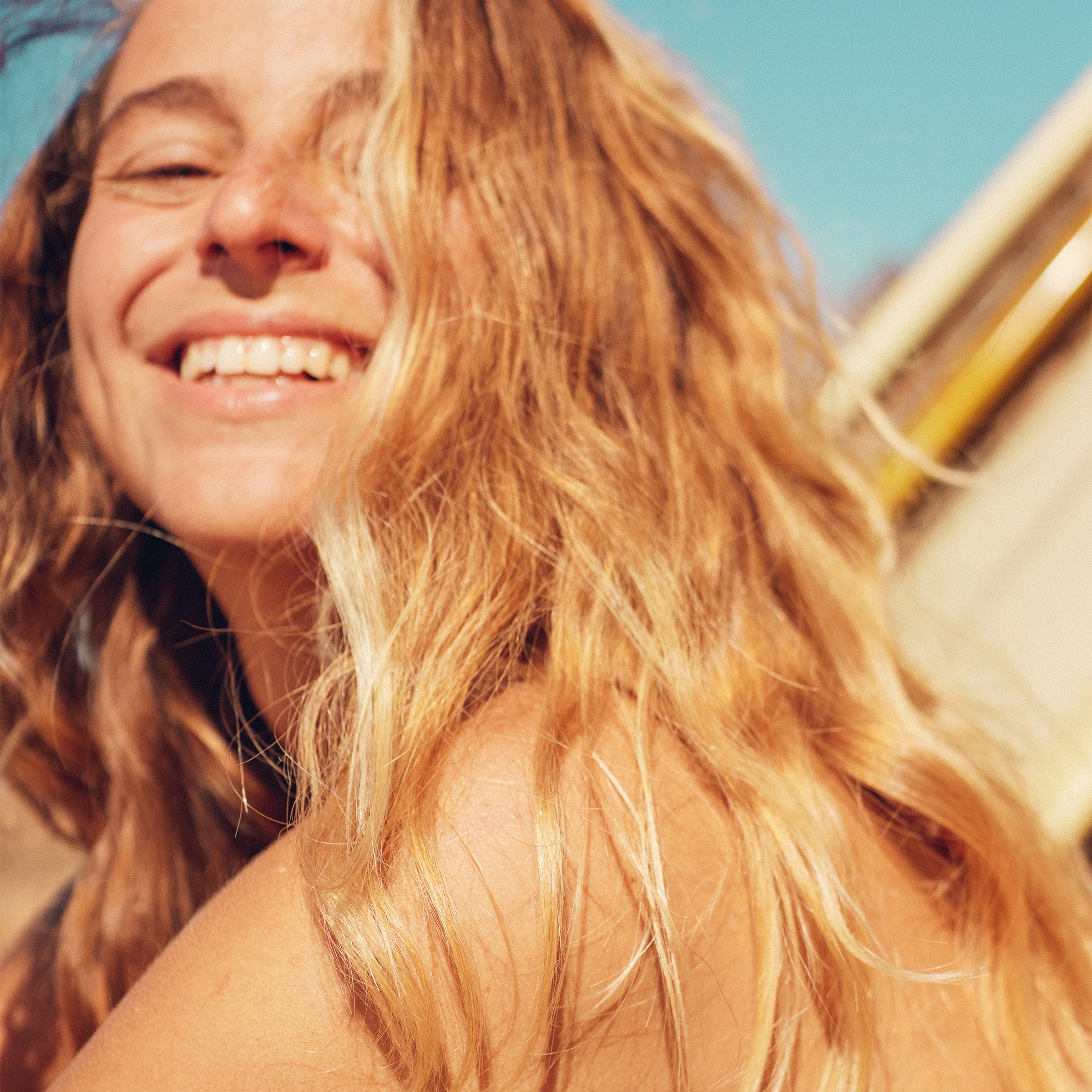 Close-up of smiling surfer girl with tousled, sun-lightened hair glowing in golden hour – Blonde Collection - Sun Bum.