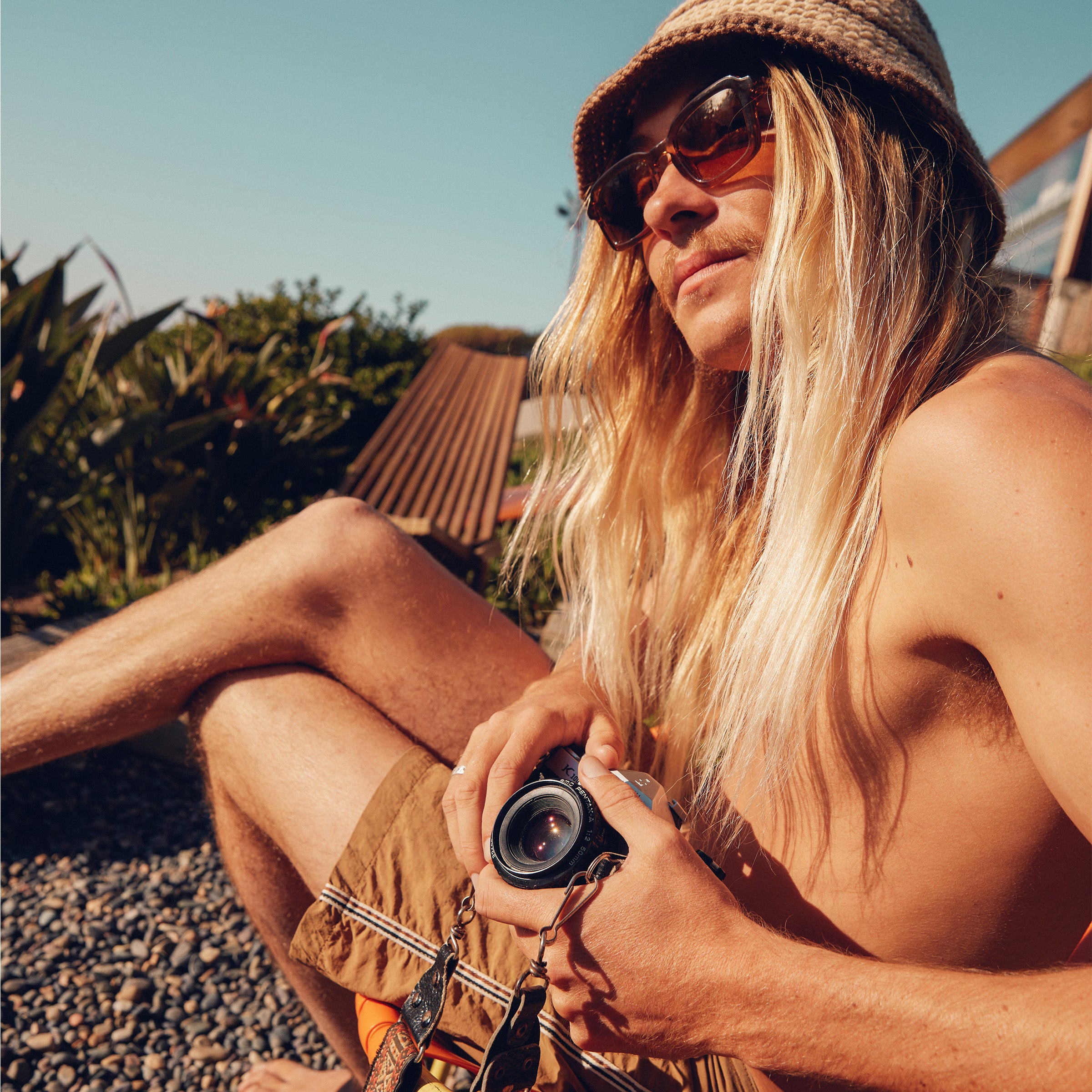 Blonde surfer chillin’ with a camera in hand, showcasing sun-kissed hair care – Blonde Collection - Sun Bum.
