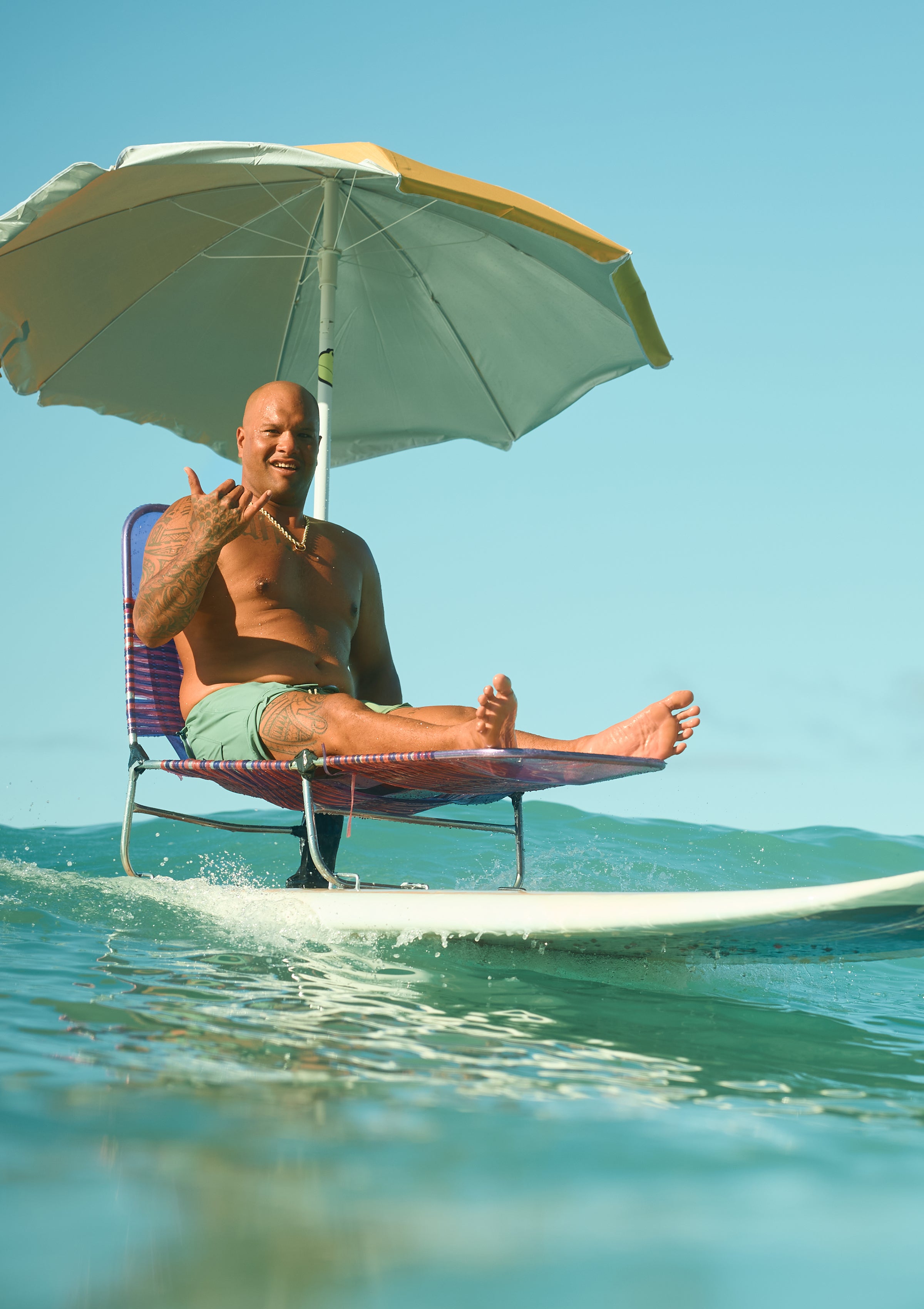 Man lounging on a surfboard chair with an umbrella, catching waves in style from the SB Sun Care Collection – Sun Bum.