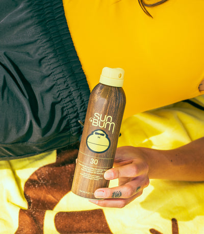 Close-up of Sun Bum SPF 30 spray sunscreen on a beach towel, part of the Regulated Shipping Collection – Sun Bum.