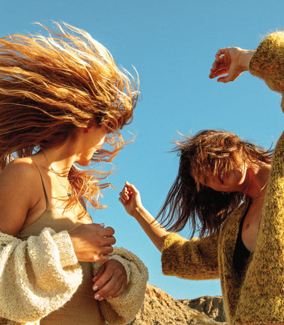 Two women dancing outdoors with textured, wind-blown hair under the sun, featuring the SB Texturizing Hair Care Collection – Sun Bum.