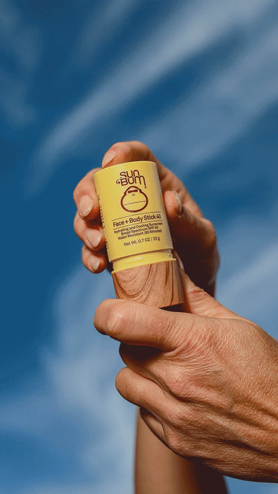 Person holding Sun Bum Face ad Body Stick 40 on blue background