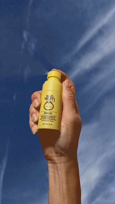 Person holding Sun Bum Mist 45 Spray on blue sky background 