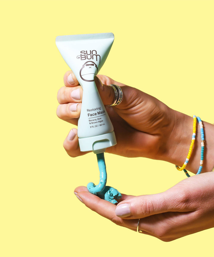 Hands holding and squeezing Sun Bum Restoring Face Mask with blue cream onto palm. Sun Bum.