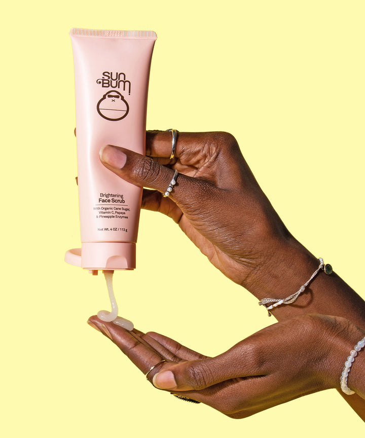 A hand squeezing Sun Bum Brightening Face Scrub with a blend of Papaya & Pineapple Enzymes and Organic Cane Sugar onto the palm, Sun Bum