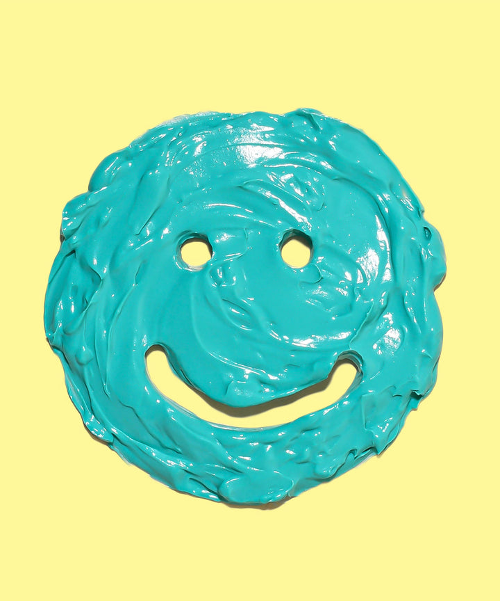Bright blue Restoring Face Mask with a smiley face design against a yellow background, featuring a soothing blend of Banana, Aloe, and Brown Algae for hydration and calming redness and irritation. Sun Bum