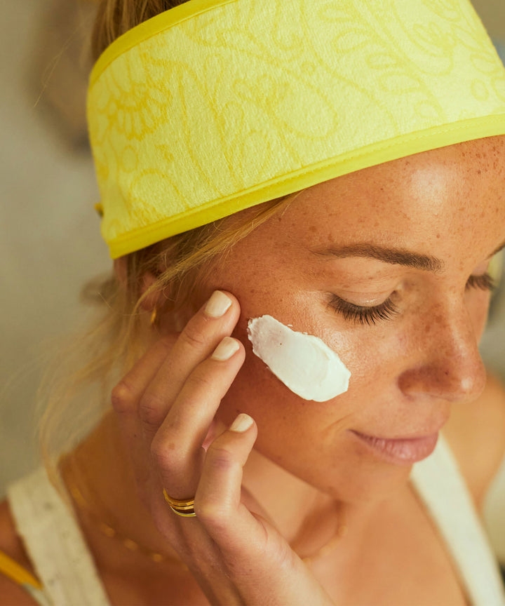 Woman applying Restoring Night Cream with antioxidant-rich Banana, Niacinamide, and Vitamin E before bedtime to nourish and soothe her skin, Sun Bum.